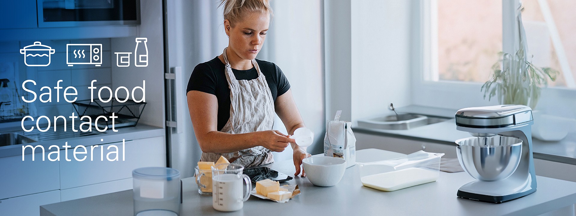 Junge Frau beim Backen in der Küche, auf der Arbeitsfläche stehen verschiedene Haushaltswaren, Haushaltsgeräte und Lebensmittelverpackungen 