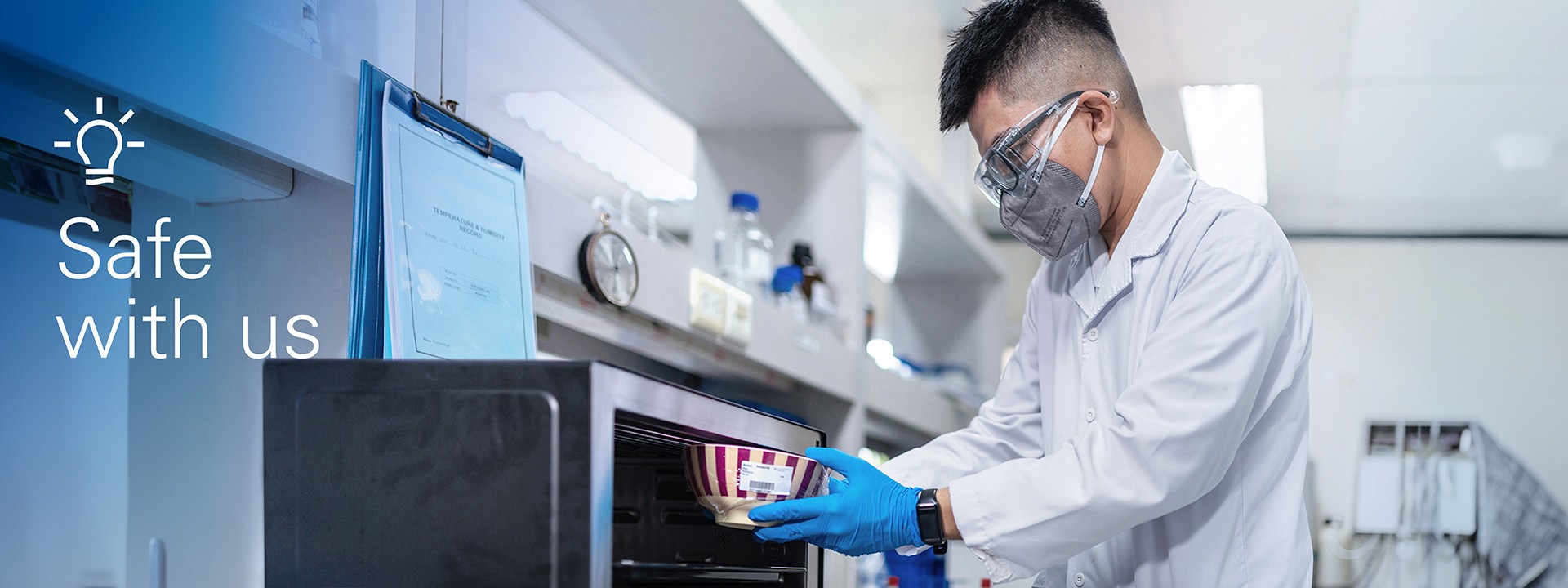A lab technician wearing a mask and safety goggles placing a dish in a microwave as part of a test for non-intentionally added substances