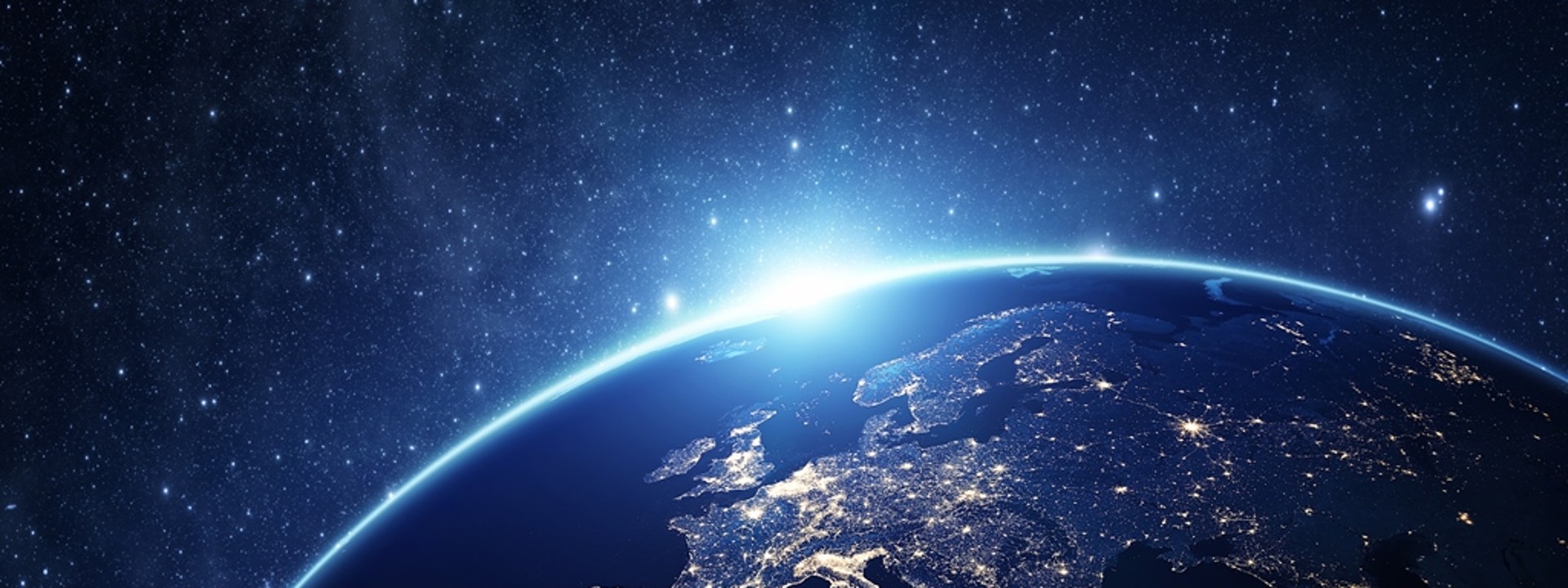 A close up of planet Earth from space, backlit with hundreds of stars. The view is pointed towards western Europe and the lights are on across the globe as if i