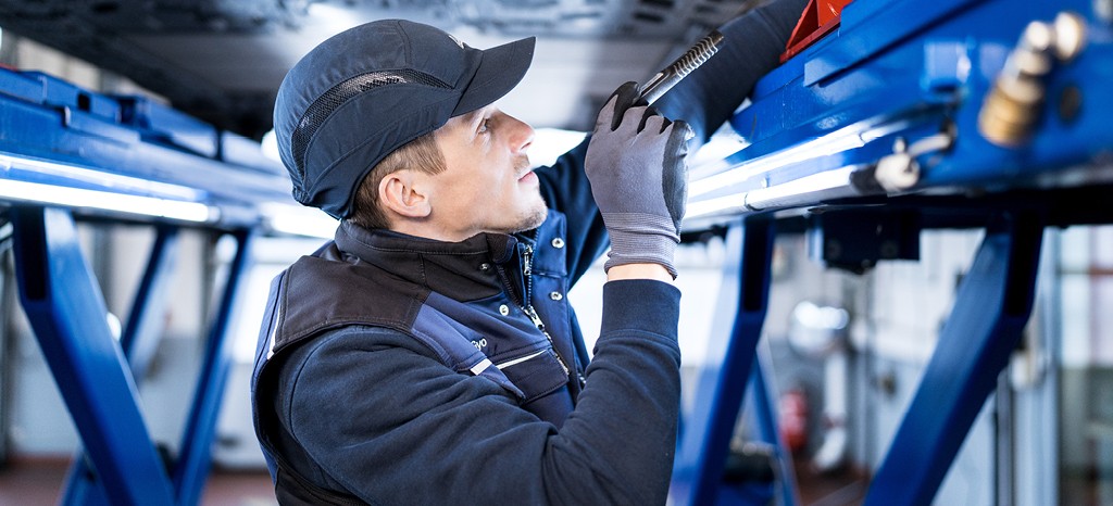 Techniker prüft Fahrzeugunterseite auf Hebebühne 