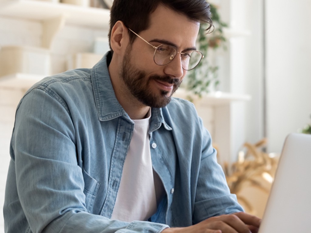 Glücklicher Mann arbeitet am Laptop mit einem Hintergrund voller Pflanzen | TÜV Rheinland