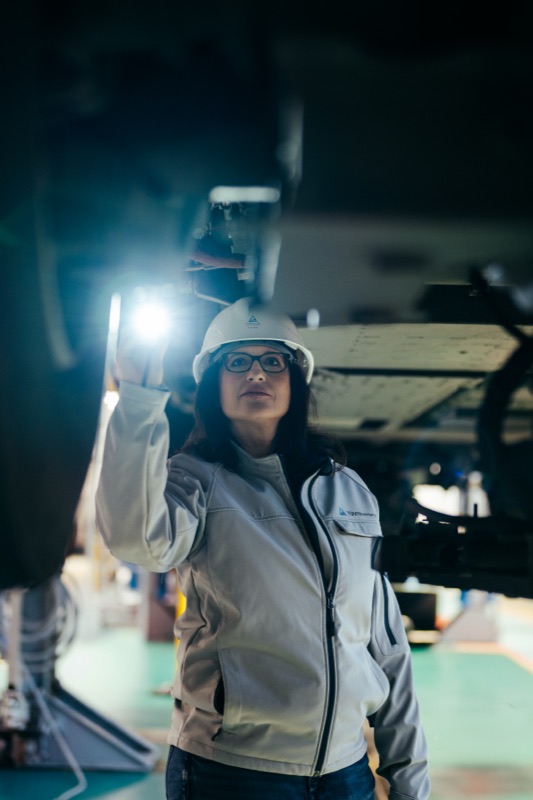 Prüfingenieurin mit Schutzhelm und Arbeitsjacke bei der Inspektion von Industrieanlagen mit einer Taschenlampe