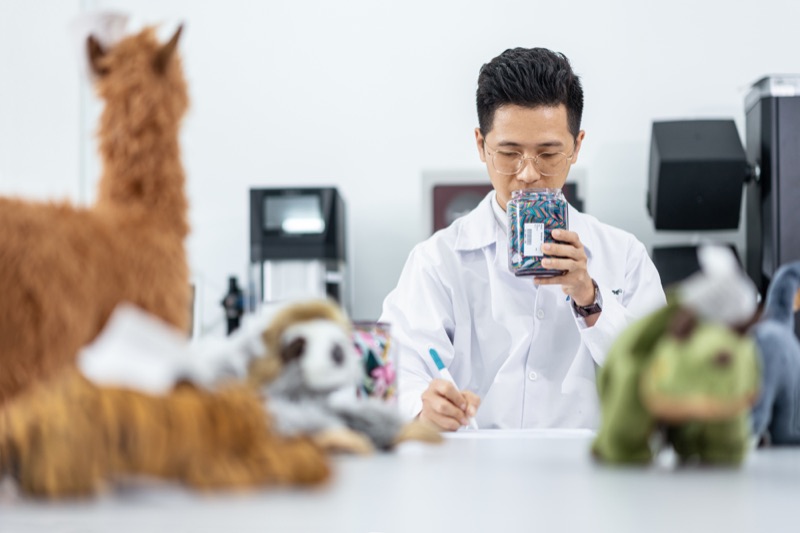 Laboratory technician in a white coat inspecting and documenting toy products at a testing facility