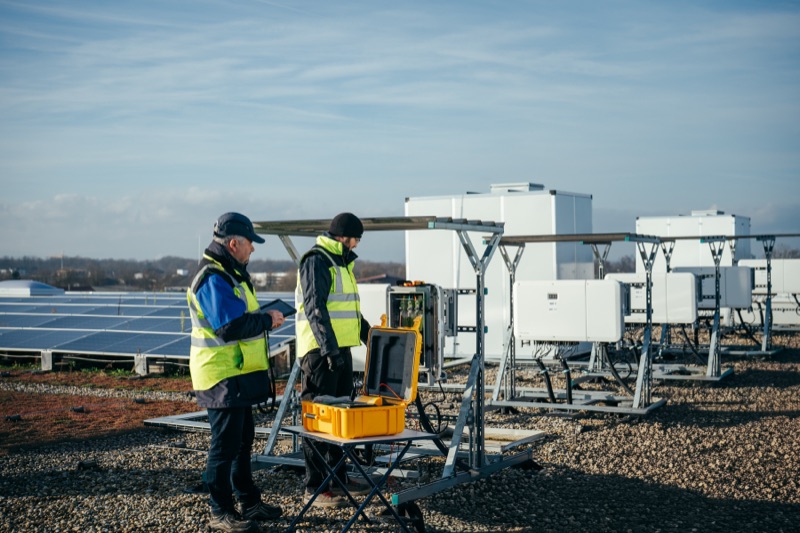 Two engineers in safety vests inspecting equipment at a solar panel installation site