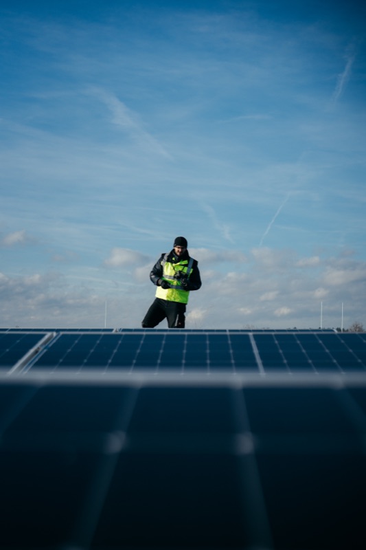 Engineer in a safety vest standing among solar panels under a cloudy sky