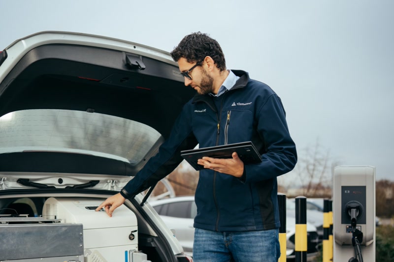 Engineer with a tablet inspecting an electric vehicle at a charging station