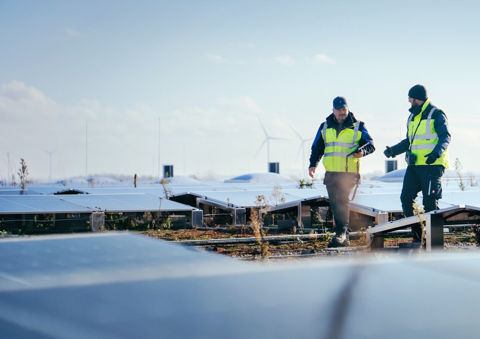 Two technicians in safety vests inspecting solar panels in winter